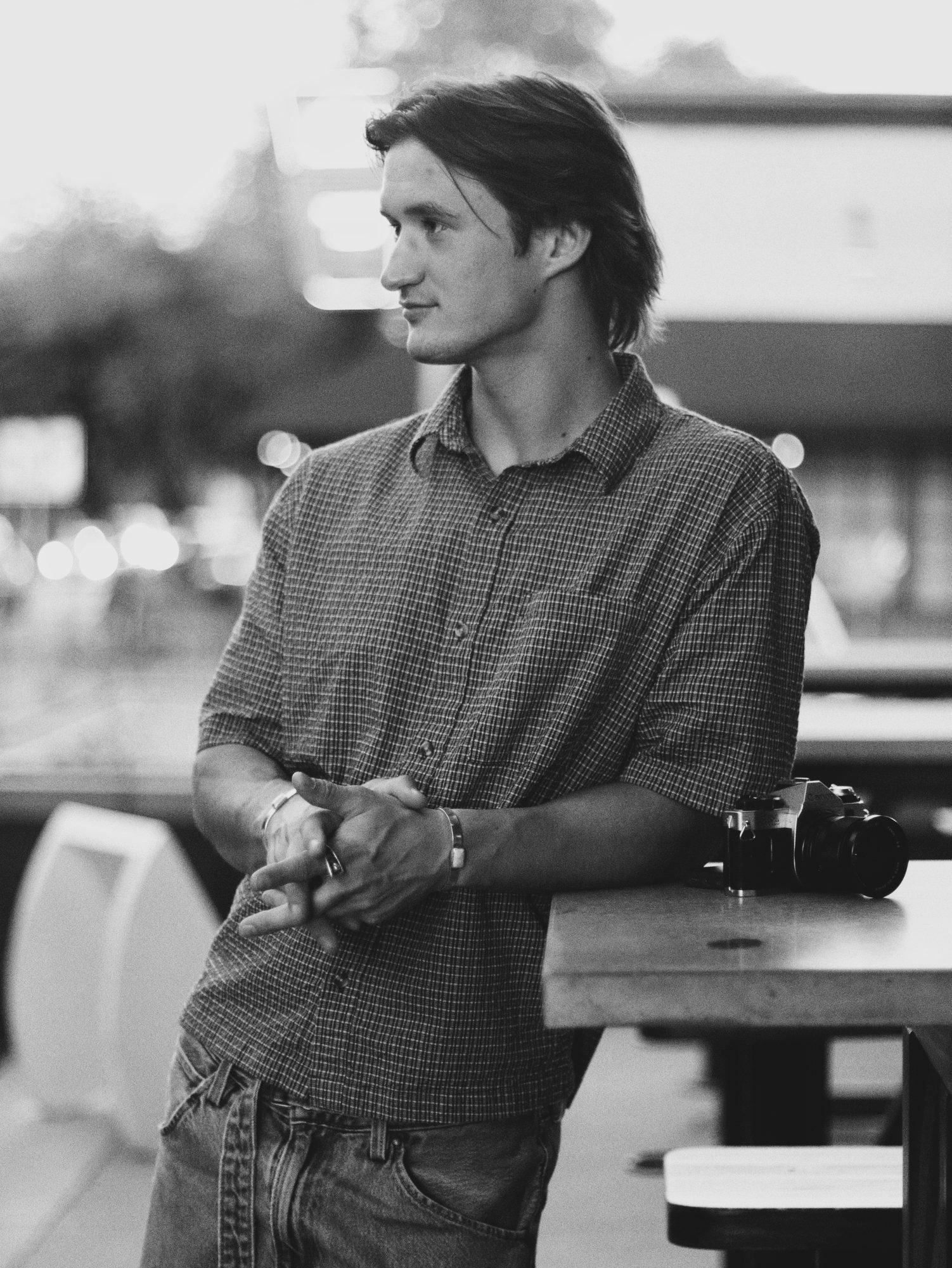 Boston leaning on a table beside a film camera, looking away