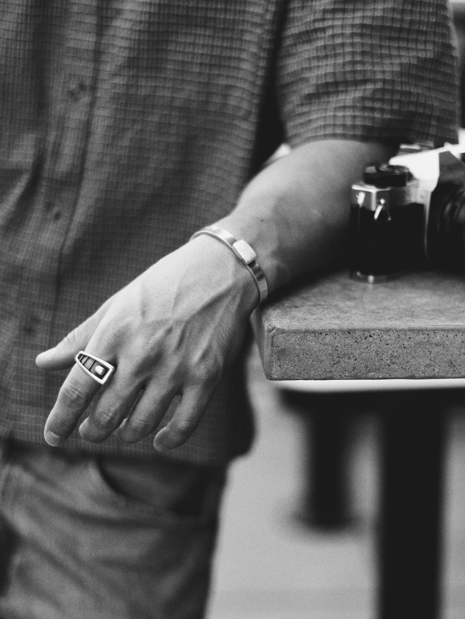 Close-up of a silver cuff and ring on Boston's hand, resting on a table by a film camera